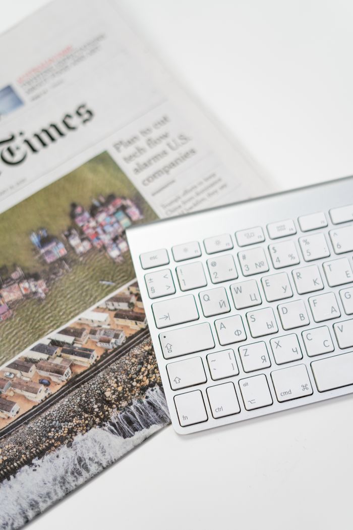 A white keyboard and newspaper on a desk, ideal for home office or freelance work environments.
